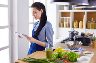 Mutfakta yemek yapmak için tablet bilgisayar kullanan genç bir kadın.