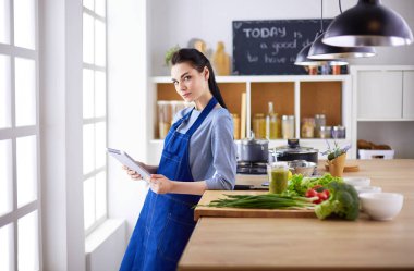 Mutfakta yemek yapmak için tablet bilgisayar kullanan genç bir kadın.