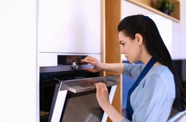 Güzel genç bayan pastasının fırında ne yaptığını kontrol ediyor.