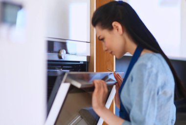 Güzel genç bayan pastasının fırında ne yaptığını kontrol ediyor.