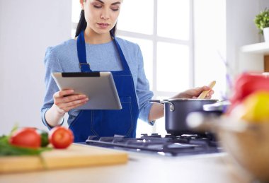 Mutfakta yemek yapmak için tablet bilgisayar kullanan genç bir kadın.