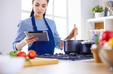 Mutfakta yemek yapmak için tablet bilgisayar kullanan genç bir kadın.