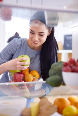 Gülümseyen kadın buzdolabından taze meyve alıyor, sağlıklı yiyecek konsepti.