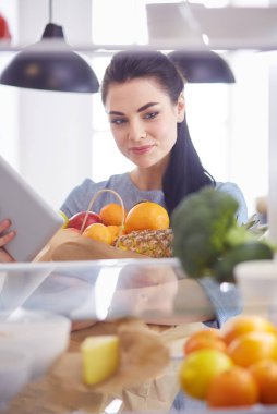 Gülümseyen kadın buzdolabından taze meyve alıyor, sağlıklı yiyecek konsepti.