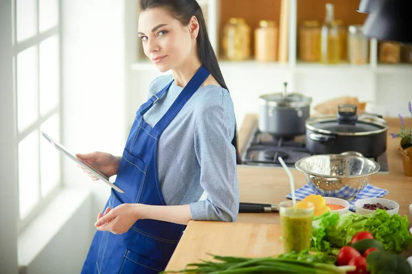 Jovem usando um computador tablet para cozinhar em sua cozinha — Fotografia de Stock