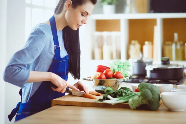 Junge Frau schneidet Gemüse in Küche zu Hause — Stockfoto