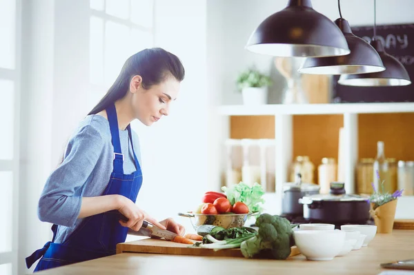 Ung kvinna skära grönsaker i köket hemma — Stockfoto