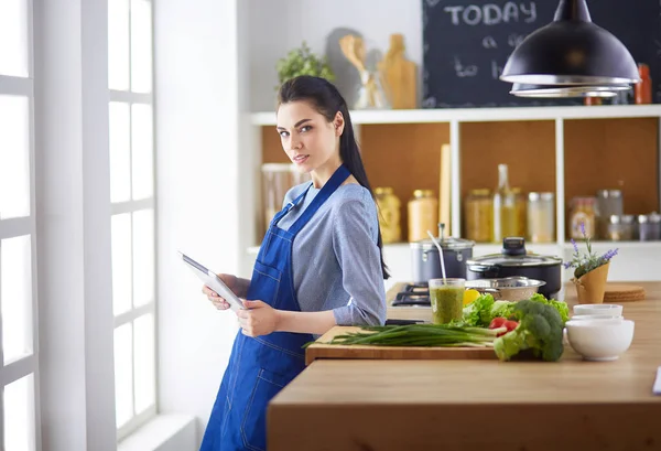 Jovem usando um computador tablet para cozinhar em sua cozinha — Fotografia de Stock