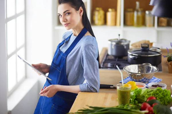 Jovem usando um computador tablet para cozinhar em sua cozinha — Fotografia de Stock