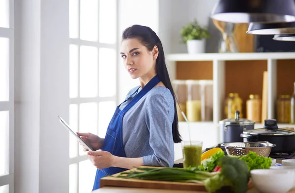 Jovem usando um computador tablet para cozinhar em sua cozinha — Fotografia de Stock