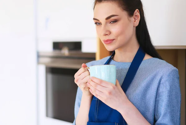 Porträtt av ung kvinna med kopp mot kök interiör bakgrund — Stockfoto