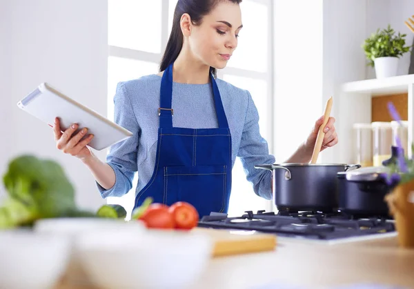 Ung kvinna använder en surfplatta dator för att laga mat i sitt kök — Stockfoto