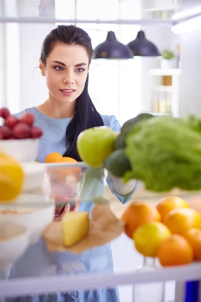 Mulher sorridente tirando uma fruta fresca da geladeira, conceito de comida saudável — Fotografia de Stock