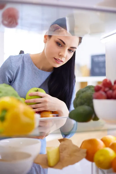 Smiling woman taking a fresh fruit out of the fridge, healthy food concept — Stock Photo, Image