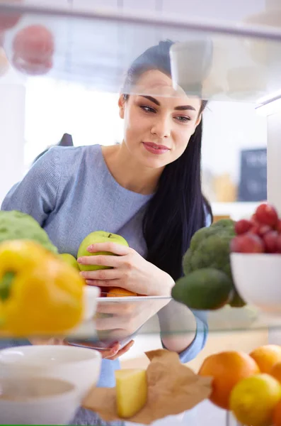 Donna sorridente che prende una frutta fresca dal frigorifero, concetto di cibo sano — Foto Stock