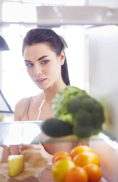 Smiling woman taking a fresh vegetable out of the fridge, healthy food concept — Stock Photo, Image