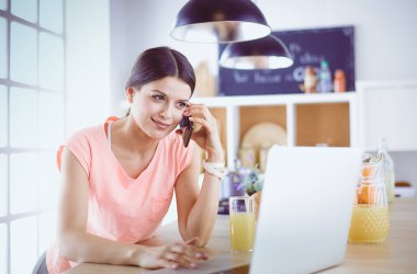 Mutfakta dizüstü bilgisayara benzeyen tariflerle gülümseyen genç bir kadın. Gıda blogcusu kavramı.