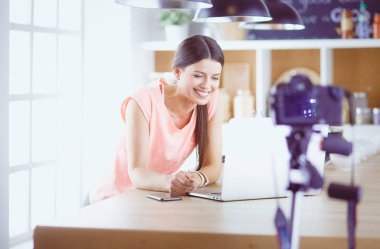 Mutfakta dizüstü bilgisayara benzeyen tariflerle gülümseyen genç bir kadın. Gıda blogcusu kavramı.