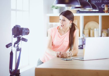 Mutfakta dizüstü bilgisayara benzeyen tariflerle gülümseyen genç bir kadın. Gıda blogcusu kavramı.