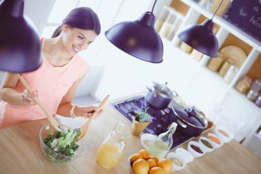 Gülümseyen genç kadın mutfakta taze salata karıştırıyor..