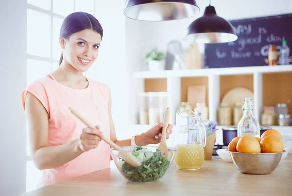 Mujer joven sonriente mezclando ensalada fresca en la cocina. —  Fotos de Stock