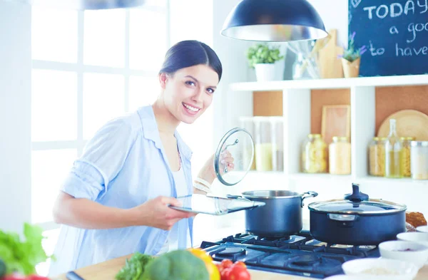 Young woman using a tablet computer to cook in her kitchen. — Stock Photo, Image