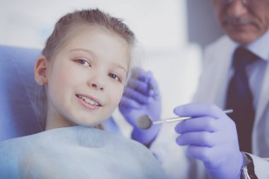 Küçük kız dişçi ofisinde oturuyor.