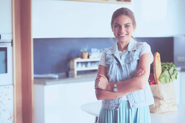 Retrato de mujer joven de pie con los brazos cruzados contra el fondo de la cocina —  Fotos de Stock