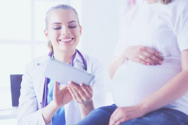 Mujer sonriente médico muestra imágenes en la tableta a la mujer joven embarazada en el hospital. — Foto de Stock