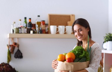 Elinde sebzeli alışveriş torbası tutan genç bir kadın. 