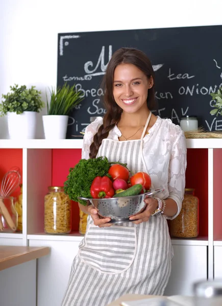 Sorridente giovane donna che tiene le verdure in piedi in cucina — Foto Stock