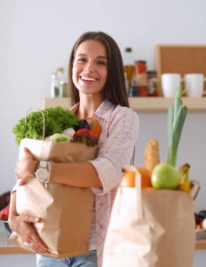 Elinde sebzeli alışveriş torbası tutan genç bir kadın. 