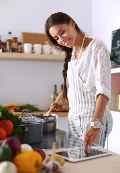 Young woman using a tablet computer to cook in her kitchen — Stock Photo, Image