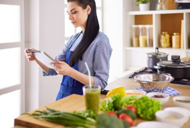 Mutfakta yemek yapmak için tablet bilgisayar kullanan genç bir kadın.
