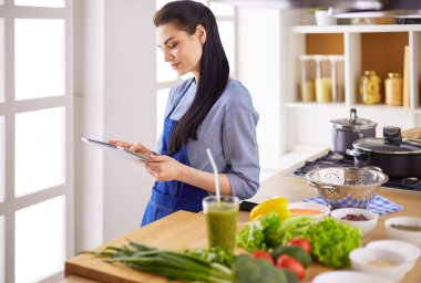 Mutfakta yemek yapmak için tablet bilgisayar kullanan genç bir kadın.