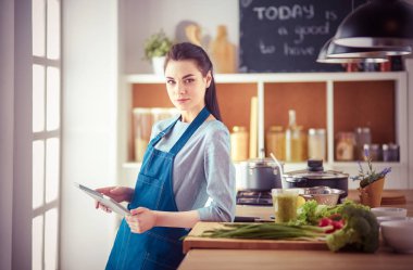 Mutfakta yemek yapmak için tablet bilgisayar kullanan genç bir kadın.