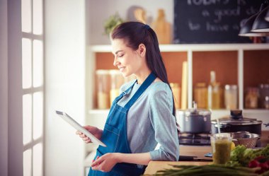 Mutfakta yemek yapmak için tablet bilgisayar kullanan genç bir kadın.