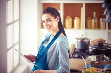 Mutfakta yemek yapmak için tablet bilgisayar kullanan genç bir kadın.