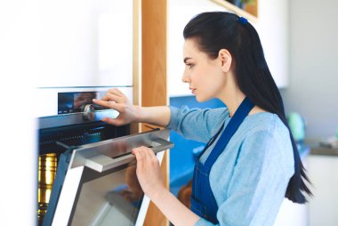 Güzel genç bayan pastasının fırında ne yaptığını kontrol ediyor.