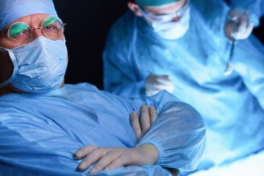 Ameliyathanede çalışan bir grup cerrah mavi tonda çalışıyor. Tıbbi ekip operasyon yapıyor.