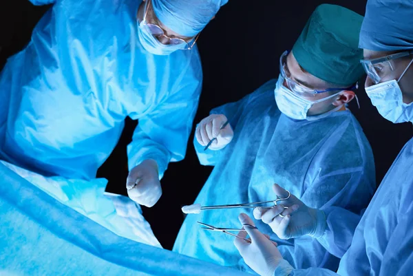 Grupo de cirujanos trabajando en quirófano tonificado en azul. Equipo médico realizando la operación — Foto de Stock