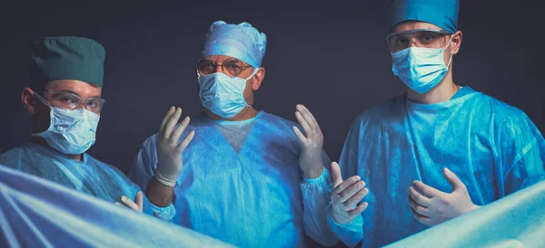 Grupo de cirurgiões no trabalho em sala de operações tonificada em azul. Equipe médica realizando operação — Fotografia de Stock