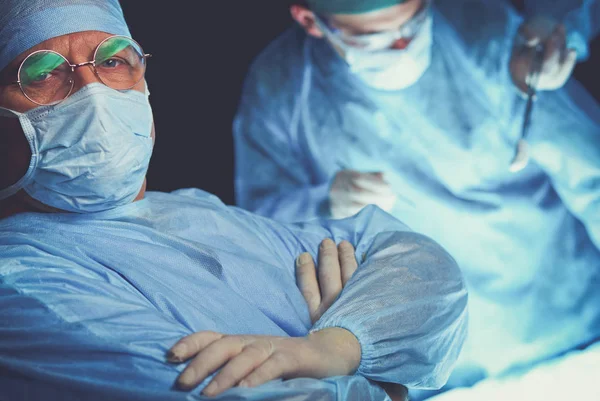 Group of surgeons at work in operating theater toned in blue. Medical team performing operation — Stock Photo, Image