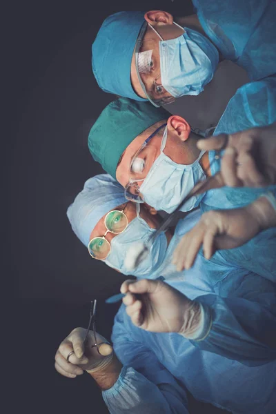 Grupo de cirurgiões no trabalho em sala de operações tonificada em azul. Equipe médica realizando operação — Fotografia de Stock