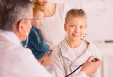Steteskoplu kız ve doktor kalp atışlarını dinliyor.