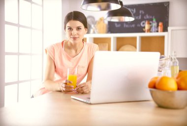 Mutfakta dizüstü bilgisayara benzeyen tariflerle gülümseyen genç bir kadın. Gıda blogcusu kavramı