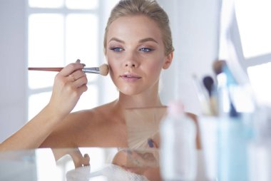 Genç bir kadının banyoya yüz pudrası sürerken fotoğrafı.