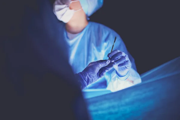 Doctor performing surgery in a dark background.