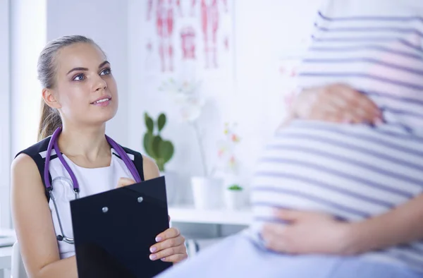 Jovem médica com estetoscópio e tablet falando com mulher grávida no hospital. — Fotografia de Stock