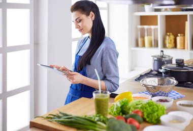 Mutfakta yemek yapmak için tablet bilgisayar kullanan genç bir kadın.